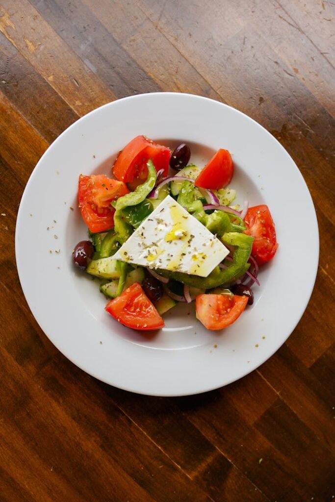 A vibrant Greek salad with feta, tomatoes, cucumber, and olives on a white plate.